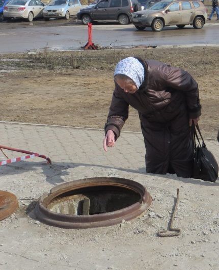 Пожилая женщина смотрит в канализационный колодец